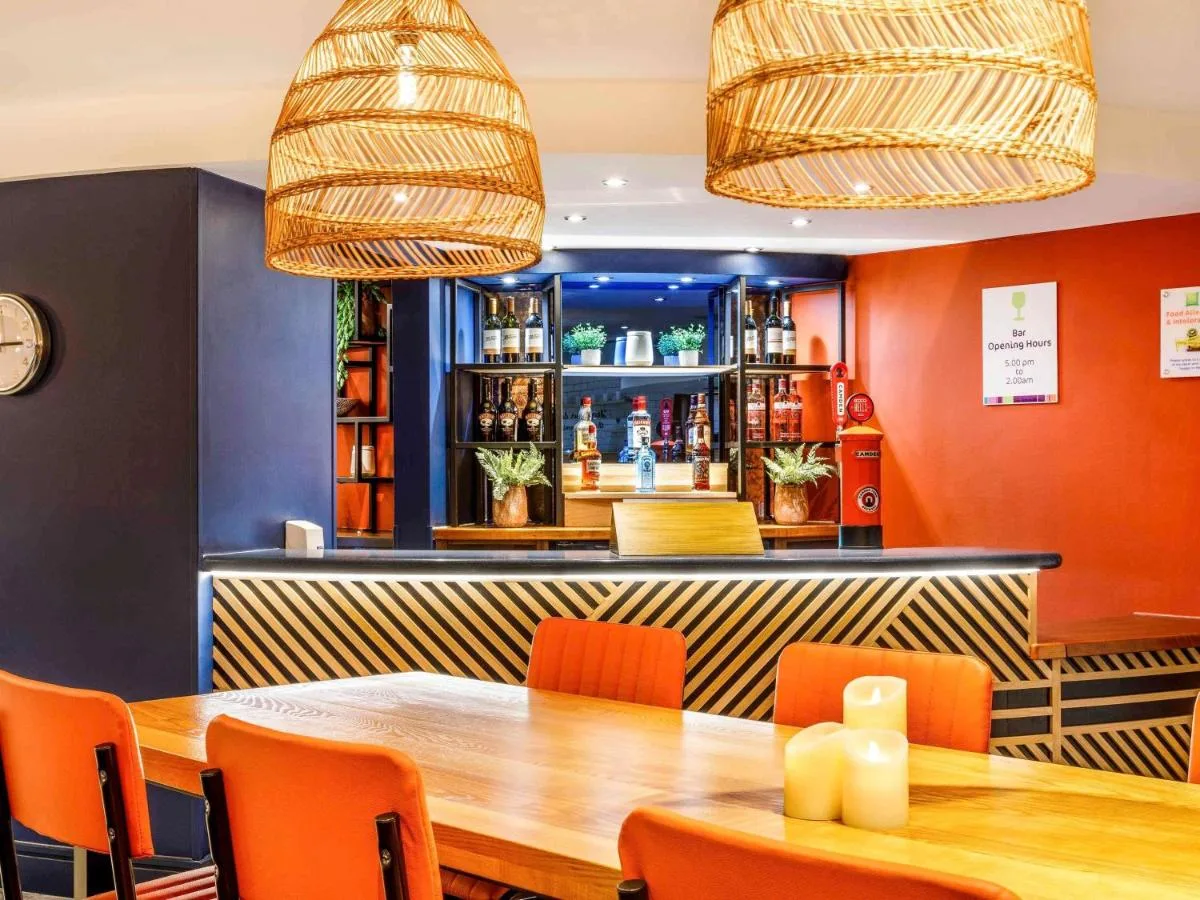 a restaurant with a wooden table and orange chairs at ibis Styles Birmingham Centre in Birmingham